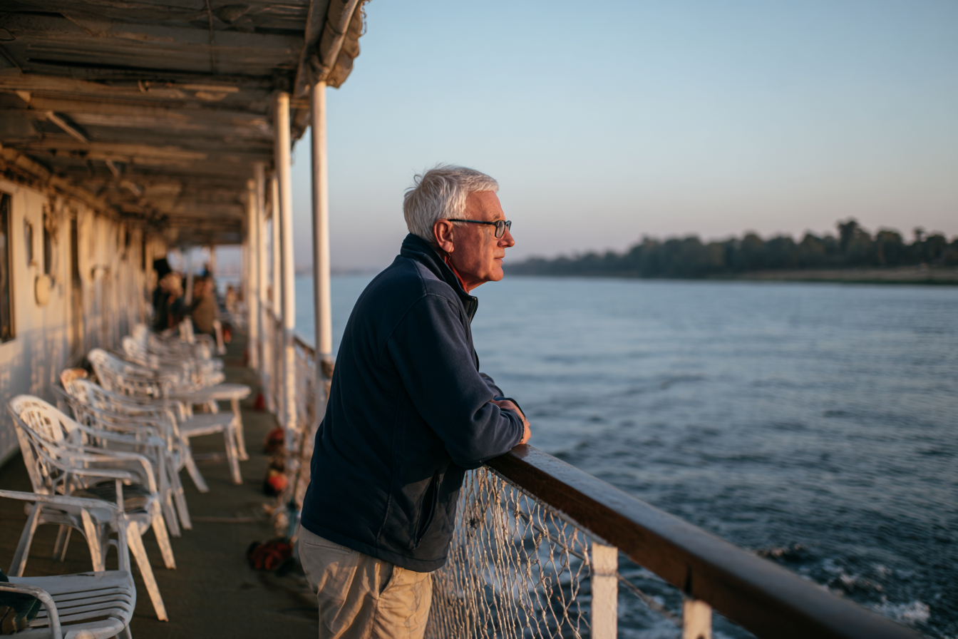 Keith on the top deck of the Nile Marquise, in a navy jacket, looking at the riverbank